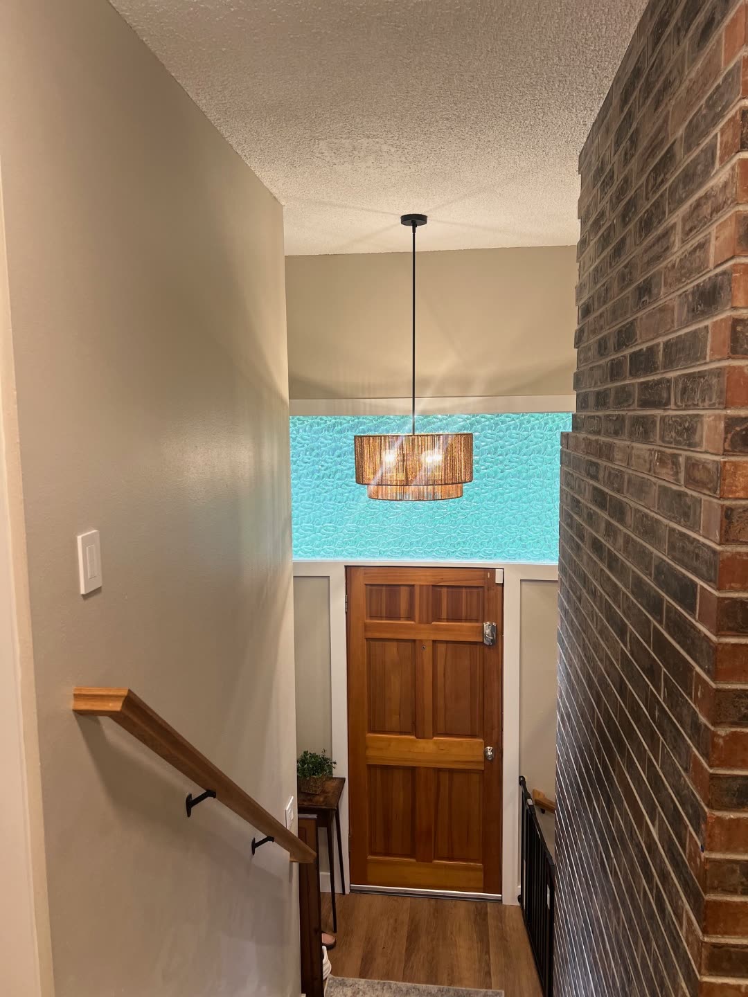 Jones entry after renovation — the rope-drum chandelier installed over the entry, with brick accent wall and teal pebble-glass partition.
