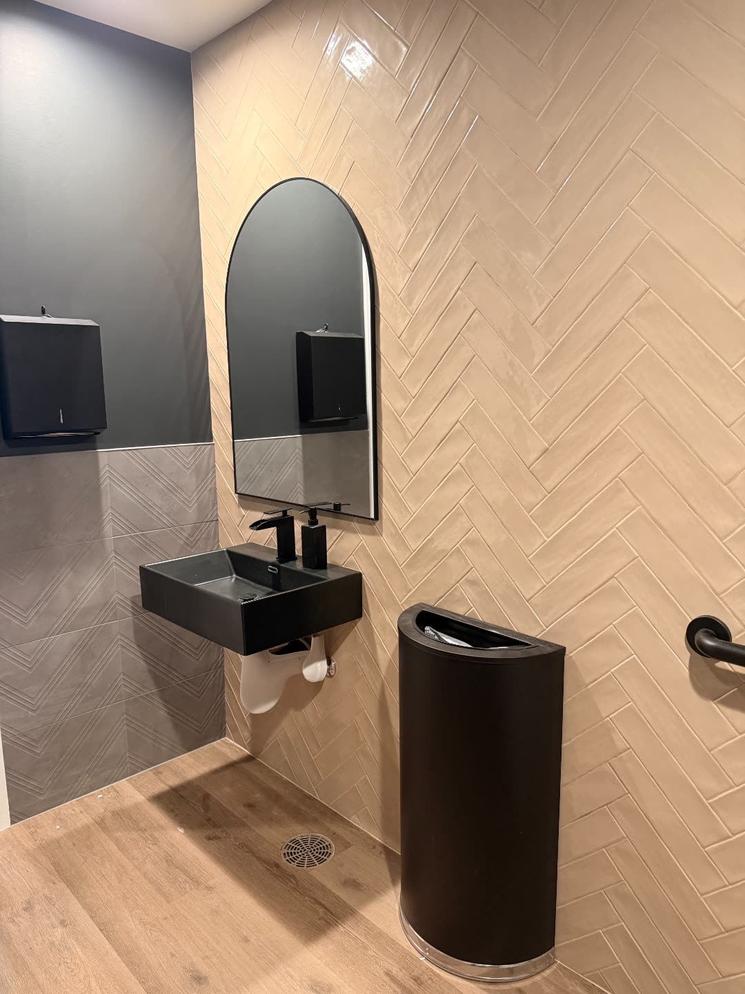 Rubicon ADA bath built — arched mirror, black wall-mount sink and herringbone tile.