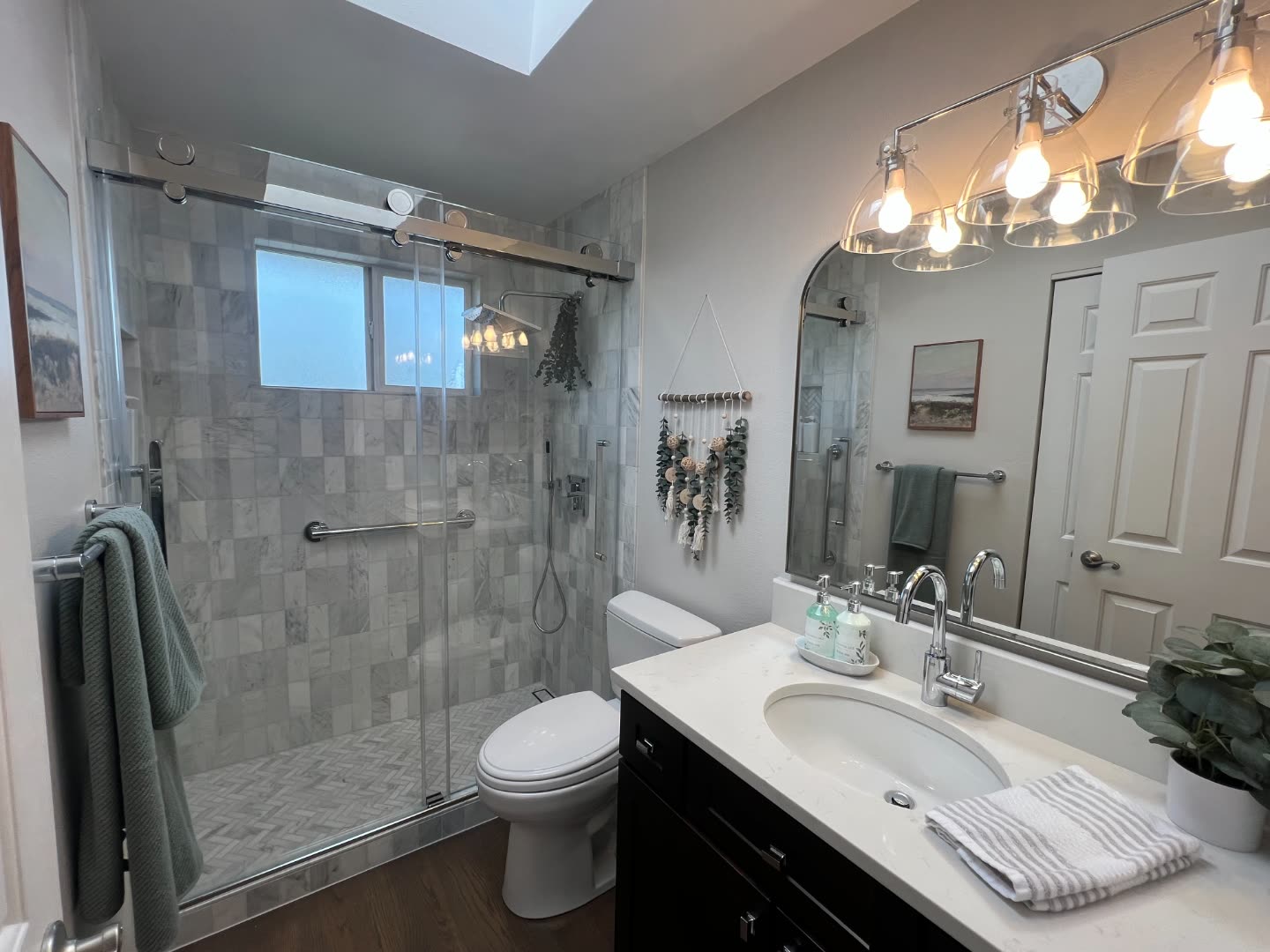 Winn primary bath after remodel — walk-in marble shower with frameless glass, herringbone marble floor, espresso vanity and seeded-glass sconces.