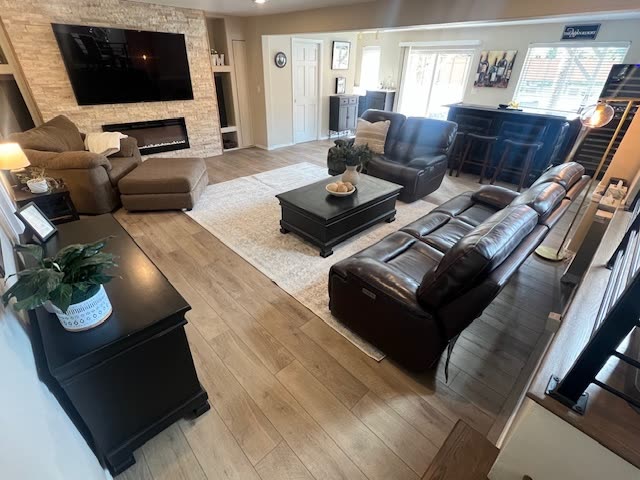 Winn living room after whole-home remodel — open-concept living with stone fireplace, wide-plank white oak LVP flooring, modern leather sectional and built-in cabinetry.