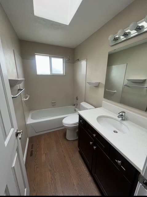 Winn upstairs bath before remodel — beige walls, white tub/shower combo, basic vanity-bar light and dark stained vanity.
