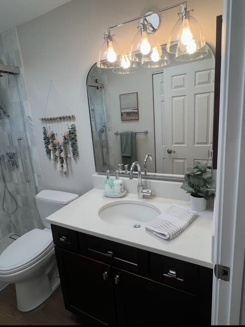 Winn upstairs bath after remodel — arched mirror, three seeded-glass globe pendants over a quartz-topped espresso vanity, marble shower visible at left.