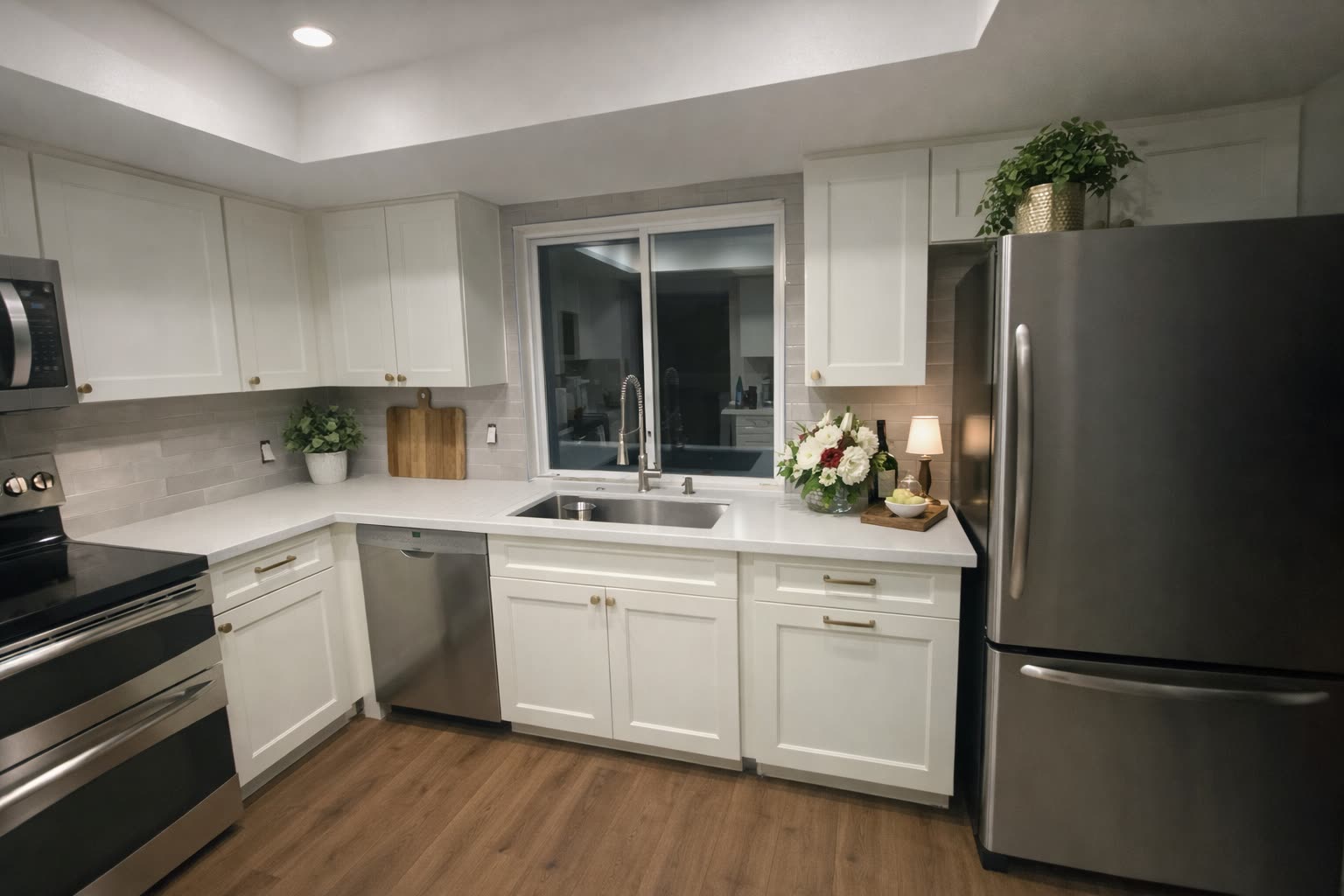Yansy kitchen after remodel — white shaker U-shape, gray subway tile backsplash, stainless appliances, garden window over the sink and tray ceiling overhead.