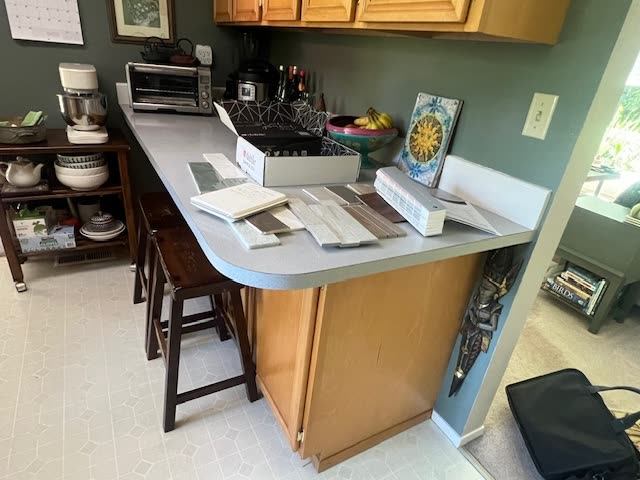 Yansy kitchen before remodel — light oak cabinetry, green walls, white laminate peninsula and dated bar stools.